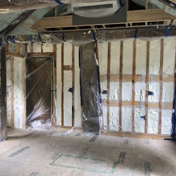 Frehill Insulation - The thickness of the wall is only 1-3/4" so Frehill suggested insulating it with open cell spray foam for a good sound barrier. - The image shows an interior room under construction, with exposed wooden wall studs and spray foam insulation applied to the wall cavities. Plastic sheeting covers certain areas, likely to protect surfaces during insulation work. The ceiling framework is visible, and a window is present on the right side, providing natural light. The floor is unfinished, and electrical outlets are installed but not yet finished. This setting indicates ongoing insulation and drywall preparation in a residential or commercial building. - Insulation Installation Near Me - Norwell, Massachusetts