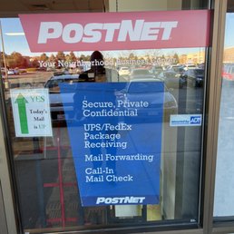 The window features a blue sign listing services such as secure mailing, package receiving, and mail forwarding at PostNet.