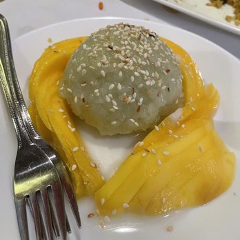 Eat At Thai - Sticky Rice Mango - A serving of mango sticky rice topped with sesame seeds, accompanied by sliced mango on a white plate, at a Thai restaurant. - Thai Near Me - Berkeley, California