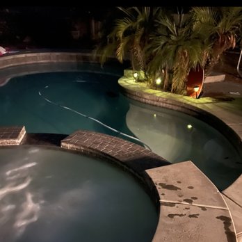 High Maintenance Pool Service - Peace of mind! The spa is also always tip top!! - Nighttime scene showing a swimming pool and hot tub with lighting, surrounded by tropical plants and a concrete deck. - Pool Cleaners Near Me