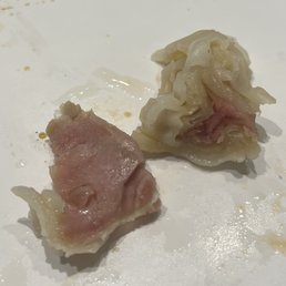 Undercooked wonton - Two dumplings with pink filling are on a white plate, one partially eaten, showing the filling and dough.