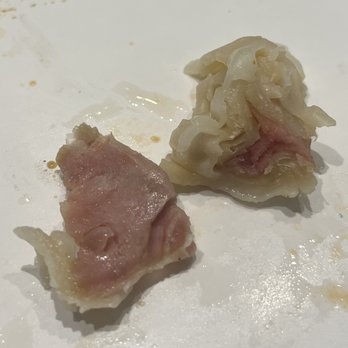 Chen Wok - Undercooked wonton - Two dumplings with pink filling are on a white plate, one partially eaten, showing the filling and dough. - Chinese Near Me - Phoenix, Arizona