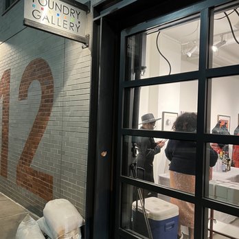Foundry Gallery - Foundry Gallery's exterior features a sign and a large brick number 12, with a view into the interior showing two people engaged with artwork. - Art Galleries Near Me - Washington, DC, District of Columbia