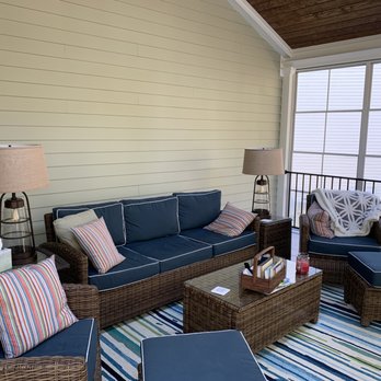 Pro-Built Construction - a patio with wicker furniture - An outdoor balcony features wicker furniture with navy cushions, striped pillows, and two lamps, with a view of neighboring houses and a wooden staircase. - General Contractors Near Me - Raleigh, North Carolina