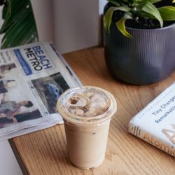 Simple Coffee - Iced coffee in between a book, newspaper, and house plants