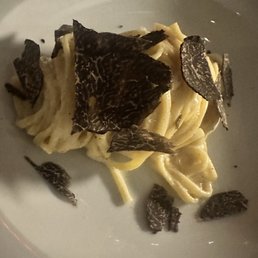 Cacio E Pepe - A serving of pasta, likely tagliolini, garnished with thin slices of black truffle, presented on a white plate.