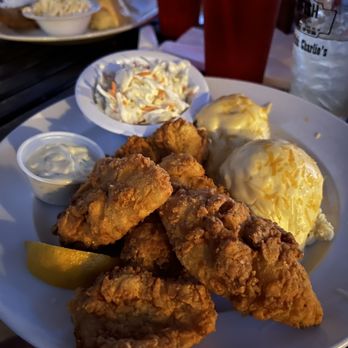 Catfish Charlie's - Bluegill - A restaurant plate features several pieces of fried chicken with a crispy coating, two baked potatoes topped with melted cheese, a small bowl of coleslaw with shredded vegetables, and a side of creamy dipping sauce. The meal is served on a white plate, with a lemon wedge visible. In the background, there are red cups and a glass of water, indicating a casual dining environment. - Seafood Near Me - Dubuque, Iowa