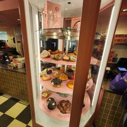 A glass display case showcases a variety of decorated donuts at Voodoo Doughnut in Denver, Colorado, with some topped with colorful sprinkles and icing.