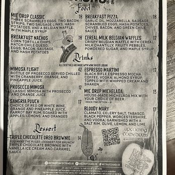 Mic Drop Comedy - The menu from Mic Drop Comedy offers a variety of brunch food and drink options, including breakfast nachos, cereal milk Belgian waffles, and breakfast pizza. Drink selections include mimosa flights, espresso martinis, and mic drop Michelada. The menu is printed in black and white with a playful design, featuring a small illustration of a microphone and a QR code for additional information. - Comedy Clubs Near Me - Chandler, Arizona
