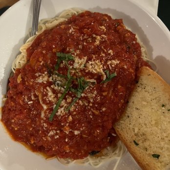 Patty B's - Chicken Parmesan - A serving of spaghetti topped with marinara sauce, garnished with grated cheese and fresh basil leaves, is presented on a white plate. A slice of garlic bread with herbs is placed on the side. The dish appears to be an Italian pasta meal, served in a restaurant setting. - Italian Near Me - Dover, New Hampshire
