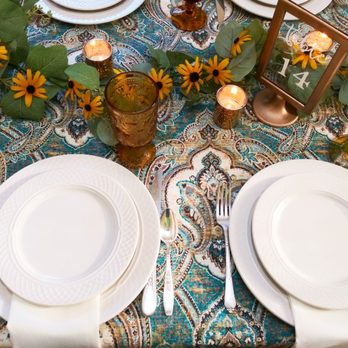 Delicate Dishes - Ivory plates and amber goblets make a beautiful contrast to this vivid table cloth. - Party Equipment Rentals Near Me Delicate Dishes - Ivory plates and amber goblets make a beautiful contrast to this vivid table cloth. - Party Equipment Rentals Near Me