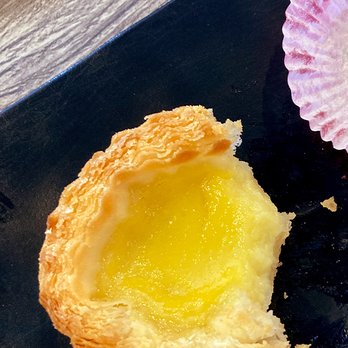 IT DIMSUM - Baked Egg Tart - A baked egg tart with a flaky, golden crust and a smooth, yellow custard filling, placed on a black surface. - Dim Sum Near Me - Albuquerque, New Mexico
