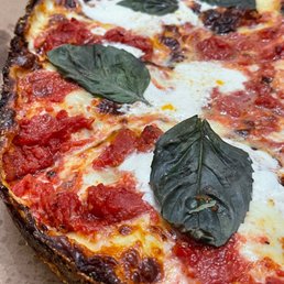 Deep Dish Pizza - A pizza topped with fresh basil leaves, melted cheese, and tomato sauce, with a slightly charred crust.