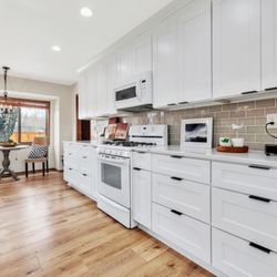 Lily Ann Cabinets - Bright kitchen featuring White Shaker Elite cabinets, sleek black pulls, a navy accent wall, and a walk-in pantry. Clean, modern, and airy!