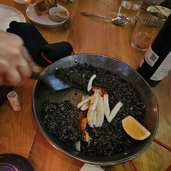 Picala - Arroz Negro: Paella dyed black with squid ink ready to be served by the waitress - Spanish Near Me - Los Angeles, California
