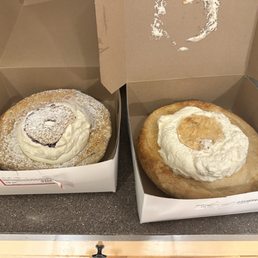 Blueberry Cream & Apple Cream - Two large bakery pastries with cream toppings are placed in open boxes on a countertop, one with a dusting of powdered sugar.