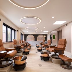 Gina Studio Estético - A pedicure area featuring brown leather chairs on raised platforms with copper pedi bowls.