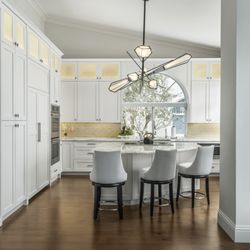 Integrative Designs - A clean, timeless Jupiter kitchen with warm wood floors, tall cabinetry, and a sculptural light fixture.