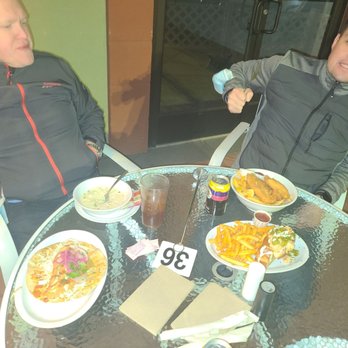 Slapfish - Two men are seated at a glass table with various dishes, drinks, and condiments in a restaurant setting. - Seafood Near Me - Albuquerque, New Mexico