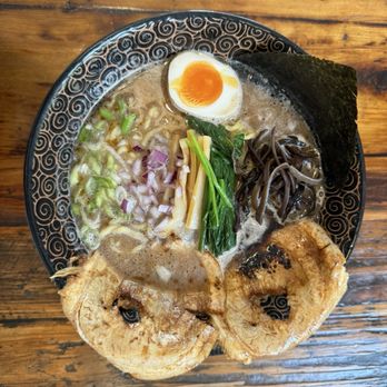 Tsuruya - Tonkatsu ramen - A bowl of ramen contains broth with various toppings including a halved soft-boiled egg, slices of pork, seaweed, chopped green onions, bamboo shoots, and black fungus. The dish is presented in a decorative black bowl on a wooden table, showcasing a variety of ingredients typical of traditional ramen. - Ramen Near Me - Berkeley, California