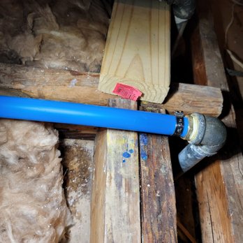 Drain Control - Great work - A blue plastic pipe is attached to a metal fitting with a hose clamp, installed among wooden framing and insulation materials. - Plumbing Near Me - Richmond, Texas