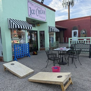 Mrs. Sprinkles Ice Cream - Exterior - The image shows the exterior of Mrs. Sprinkles Ice Cream Parlor with outdoor tables, chairs, and a cornhole game on the pavement. - Ice Cream & Frozen Yogurt Near Me - Albuquerque, New Mexico