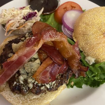 Joe's Dining - Triple B Burger - A burger topped with bacon and blue cheese, served on a bun with lettuce, accompanied by coleslaw, tomato, onion, and a small container of sauce. - Pizza Near Me - Santa Fe, New Mexico