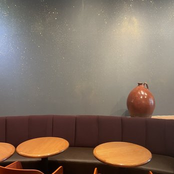 Satellite Coffee - A large, brown ceramic vase is positioned on a ledge behind a curved booth with purple upholstery, with wooden tables and orange chairs in the foreground. - Coffee & Tea Near Me - Albuquerque, New Mexico