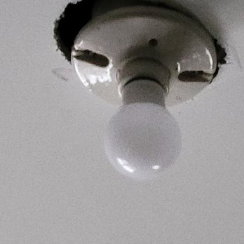 ML Painting - Final appearance of hole cut in sheetrock for light fixture - A ceiling light fixture with a bulb installed, visible through a hole in the ceiling drywall. - Painters Near Me