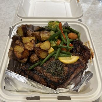Gary's Place - Steak, potatoes and vegetables! - A white takeout box contains grilled steak, roasted potatoes, and a mix of steamed vegetables including broccoli, carrots, and green beans. - Bars Near Me - West Bend, Wisconsin