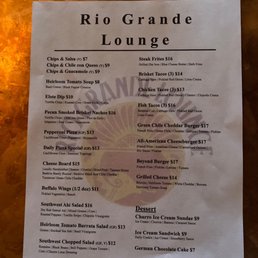 Menu - The menu from Rio Grande Lounge displays a variety of food and drink options, including chips and salsa, steak fries, tacos, pizzas, burgers, salads, and desserts. Prices range from $7 to $17, with detailed descriptions of ingredients and preparation methods. The menu is printed on a single sheet of paper with a simple layout, listing items in categories such as appetizers, main courses, and desserts.