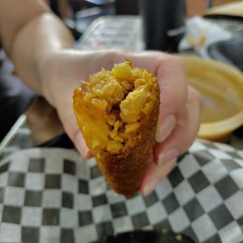 Phoenix Coqui - Inside the alcapurra vegana de yuca - A person holds a half-eaten vegan yuca empanada with a golden-brown crust, showing the yellow filling inside, at a restaurant table. - Puerto Rican Near Me - Phoenix, Arizona