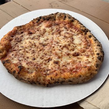 dōp Pizza - Cheese - A cheese pizza with melted cheese and a slightly burnt crust is placed on a white paper plate on a wooden table. - Pizza Near Me