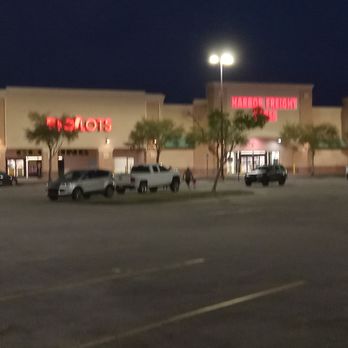 Big Lots - A parking lot at night in front of a shopping plaza features several parked vehicles, including trucks and cars. The plaza has multiple storefronts with illuminated signs, including a Target store with its red logo and other stores with lit signage. Trees line the front of the stores, and streetlights illuminate the area. The sky is dark, indicating it is after sunset. - Department Stores Near Me - Saint Augustine, Florida