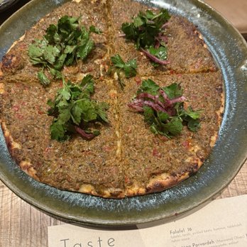 Rumis Kitchen - Lahmacun - Lahmacun, a Turkish-style flatbread topped with minced meat and herbs, is served on a ceramic plate with fresh parsley and cilantro garnishes. - Persian/Iranian Near Me - Houston, Texas