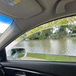 A view of the lake and a side mirror view of the greenery and park benches.