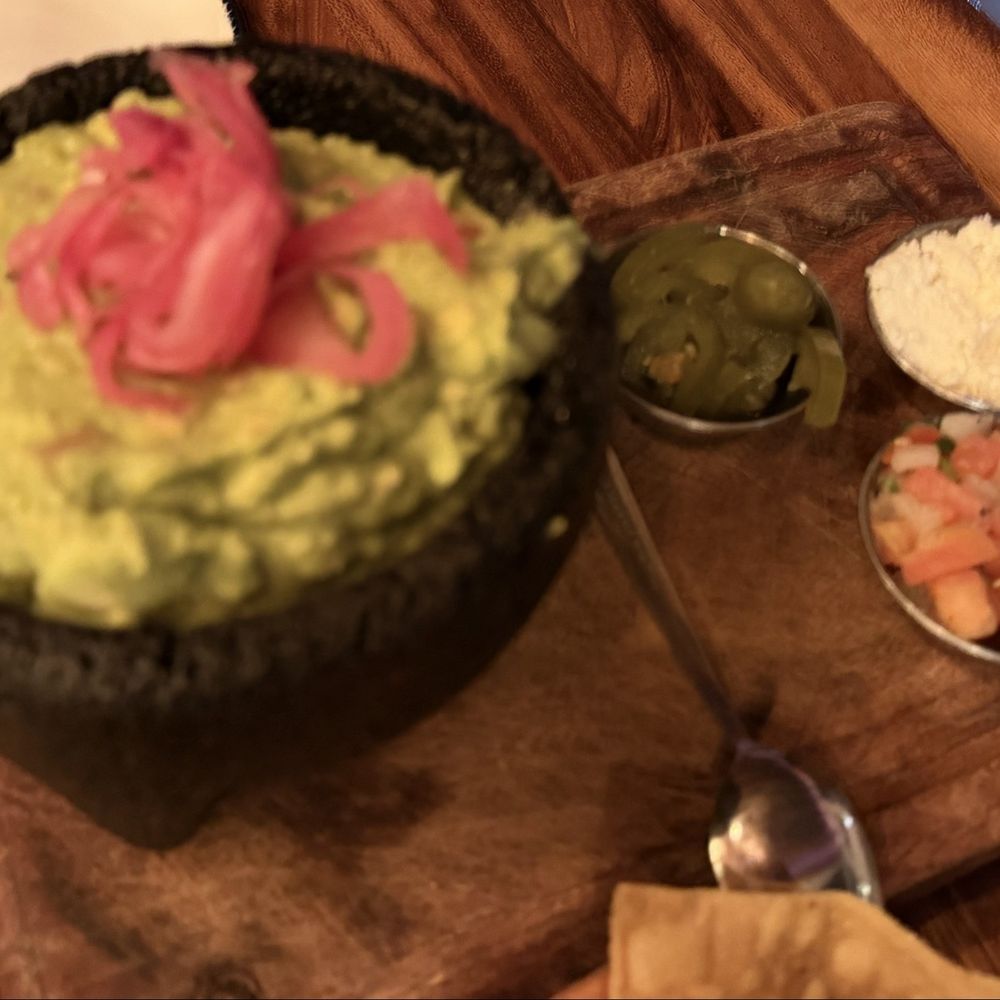 Guacamole accompanied by pickled onions, jalapeños, pico de gallo, and Cotija cheese.