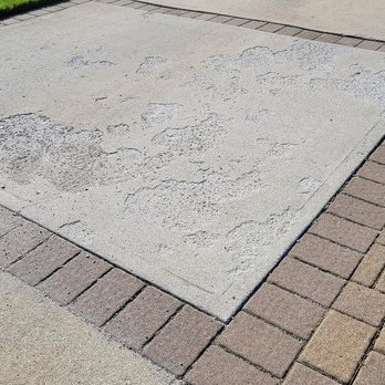 Elite Masons - Driveway - Concrete driveway with signs of wear and patches, bordered by brick and concrete pavers, with grass visible at the edge. - Masonry/Concrete Near Me - Hempstead, New York