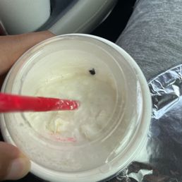 ows a person holding a plastic cup with a red straw