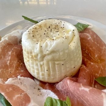 Nova Pizzabar - A dish featuring a wheel of burrata cheese topped with black pepper, accompanied by slices of prosciutto and fresh basil leaves. - Pizza Near Me - Larchmont, New York