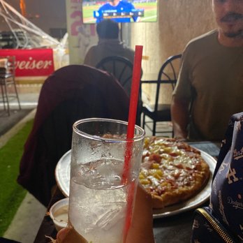 Gardens Bar & Grill - a person holding a drink and a pizza - Sports Bars Near Me - Pico Rivera, California