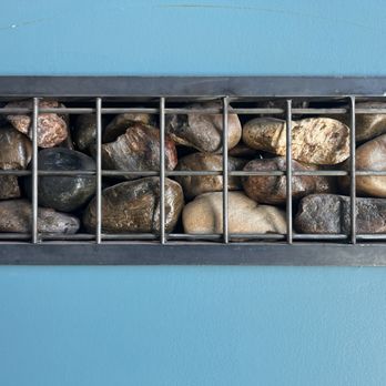 The Kosmos - Gabion not sure of spelling - Rocks of various sizes and colors are contained within a metal cage mounted on a blue wall. - Bars Near Me - Albuquerque, New Mexico
