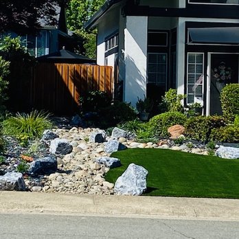 Ledgestone Landscapes - Front yard filled with color from the black slate stones to the flowering plants that surround the green artificial turf - Landscaping Near Me