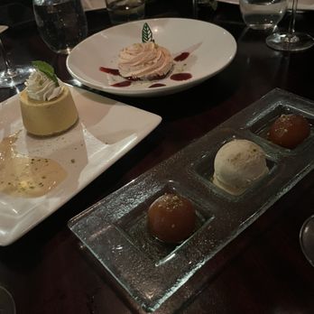 Rasika - Desserts - Three dessert dishes are shown: a mousse with a mint leaf, a whipped cream-topped dessert with red sauce, and a trio of small confections on a glass plate. - Indian Near Me - Washington, DC, District of Columbia