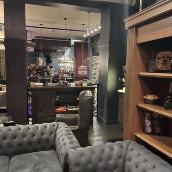 Escape Manor - A lounge with gray tufted sofas in the foreground, overlooking a restaurant or bar area with hanging lights and people dining. - Escape Games Near Me - Toronto, Ontario