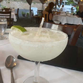 Casa Luis - Coconut Margarita - A margarita in a large glass with a salted rim, lime wedge, and straw, served at a restaurant with white tablecloths and ambient lighting. - Spanish Near Me - Smithtown, New York