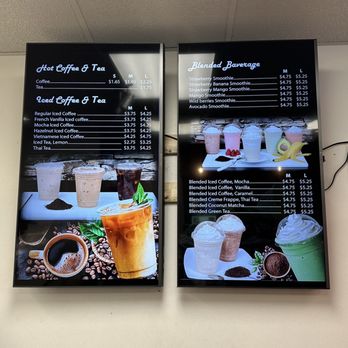 Nom Donuts - Drink menu - Digital menu boards list coffee, tea, and smoothie options with prices, accompanied by images of beverages and fruits. - Donuts Near Me - Houston, Texas