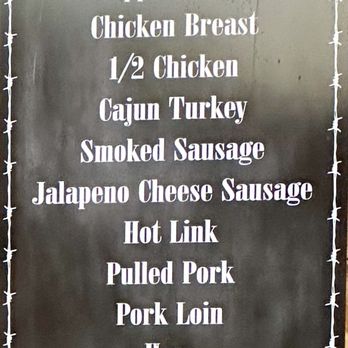 Bartley's Bar-B-Que - A vertical black menu board features white text listing barbecue options such as sliced brisket, chopped brisket, chicken breast, half chicken, Cajun turkey, smoked sausage, jalapeno cheese sausage, hot link, pulled pork, pork loin, ham, pork ribs, and smoked bologna. The board is decorated with a barbed wire border and has a small logo at the bottom. The top part of the board shows a partially visible red sign with the words 'Barbecue' and some decorative horns. - Barbeque Near Me - Grapevine, Texas