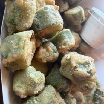 Duke City BBQ - The image displays a pile of battered and frozen jalapeño peppers, coated in a light layer of batter, with some green jalapeño pieces visible through the coating. A small container of dipping sauce is positioned to the right side of the pile. The peppers are arranged on a surface, likely for preparation or serving. - Barbeque Near Me - Albuquerque, New Mexico