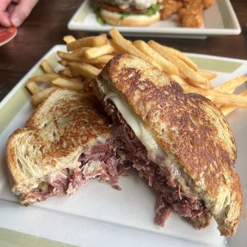 The Tap - A grilled Reuben sandwich with melted cheese and corned beef is cut in half and served with French fries on a white plate. - Pubs Near Me - Cumberland, Rhode Island